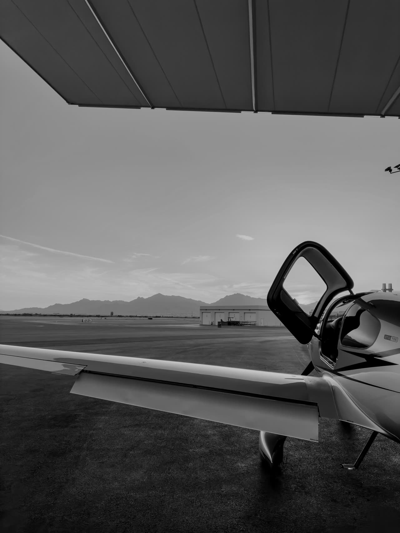 Cirrus wing and open door at sunset on a desert ramp with mountains beyond
